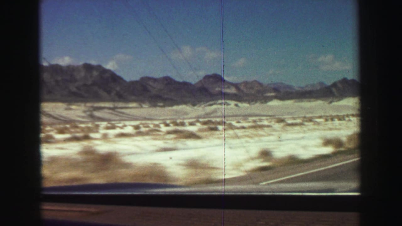 Desert plain and distant mountains seen through a dark car window frame.