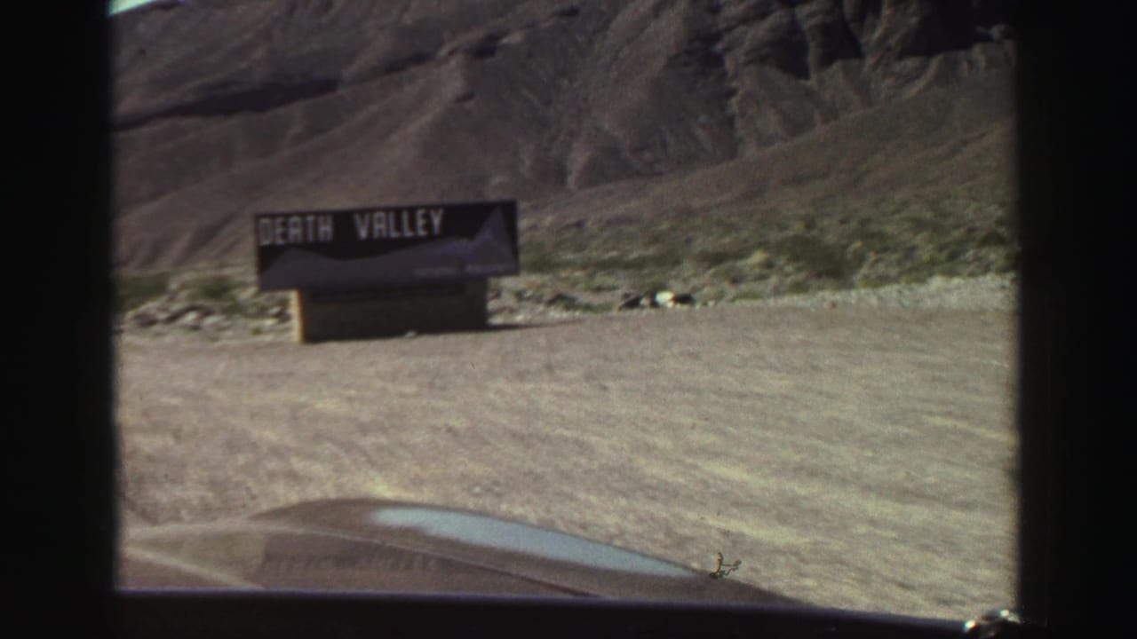 Death Valley sign beside a dusty roadside with rocky desert hills behind it.