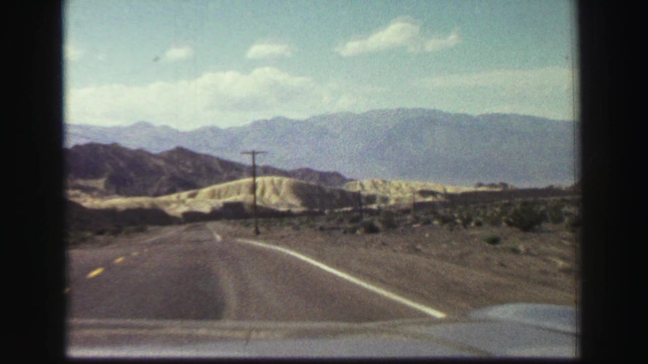 Two-lane road curves through dry hills with distant mountains and a utility pole ahead.