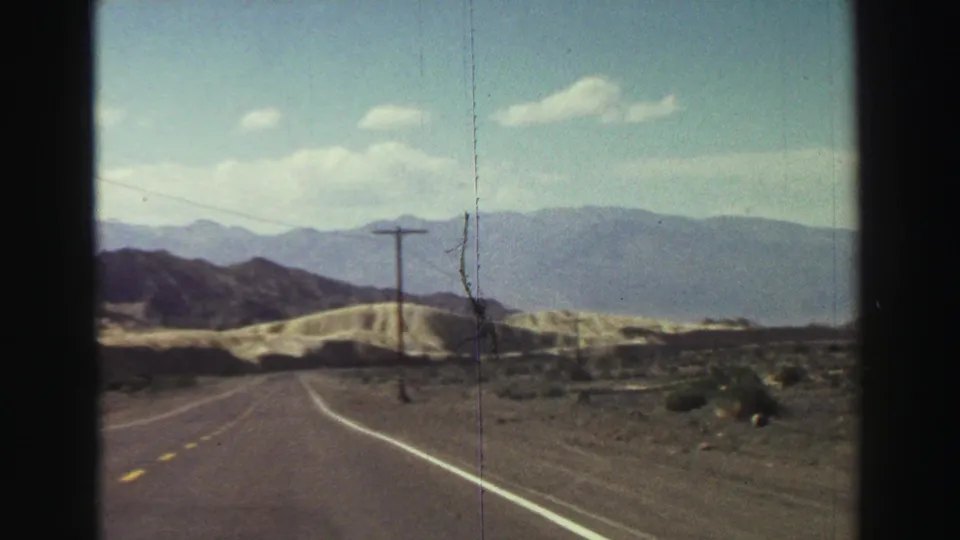 Windshield view from the 1969 8mm clip shows a curving rural road near Lake Tahoe with utility poles, arid terrain, and hazy mountains.