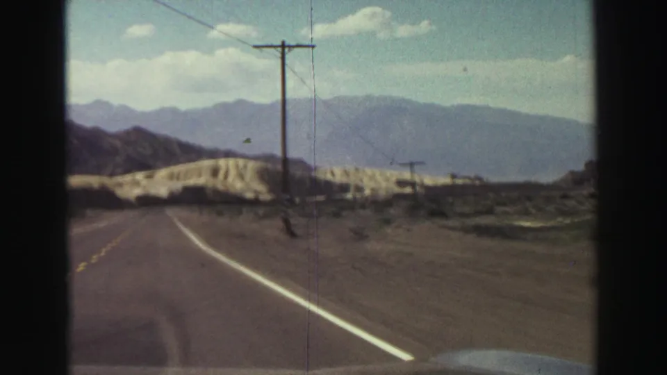 A 1969 8mm driving frame near Lake Tahoe shows a telephone pole close to the road, pale hills, desert brush, and a broad mountain backdrop.
