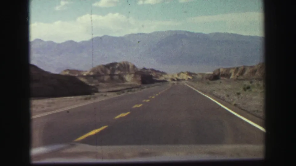Windshield view from the 1969 Lake Tahoe-area home movie shows a straighter road segment leading through dry hills toward distant mountains.