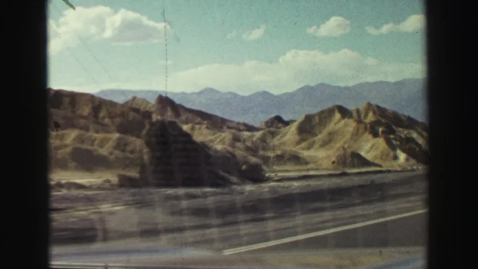 Passenger-side 8mm view of rugged hills and distant mountains beside a roadway during the supplied 1969 Lake Tahoe, California trip.