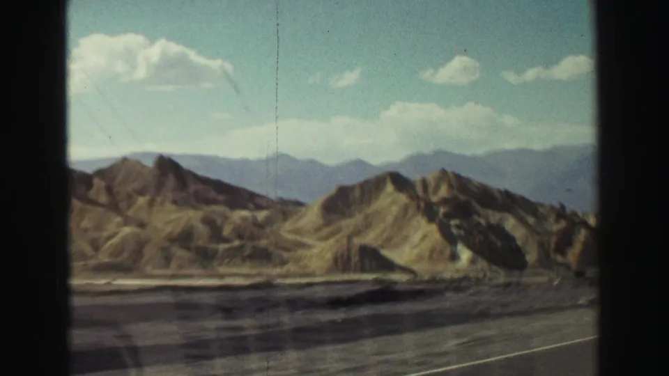 1969 8mm road-trip view near Lake Tahoe, California, showing arid hills, distant mountains, and highway pavement from a moving vehicle.