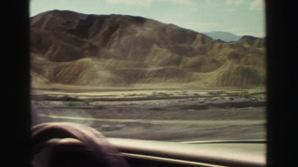 Passenger or driver-side 8mm view near Lake Tahoe in 1969, with dry hills outside and part of the car interior visible at the bottom edge.
