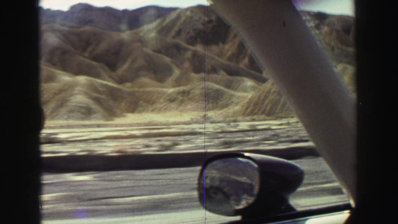 Car side window and mirror frame dry hills along the roadside.