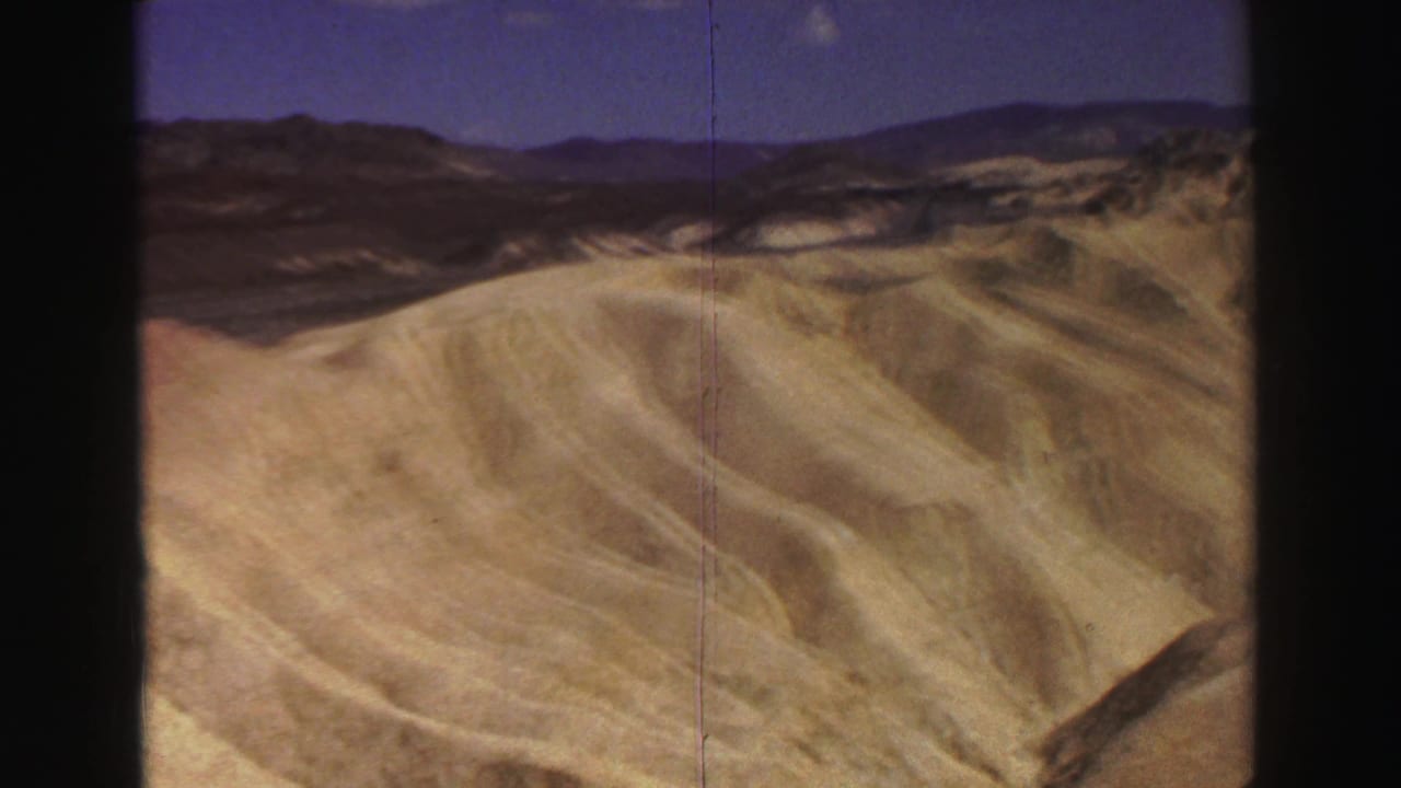 1969 8mm Lake Tahoe-area footage showing pale eroded slopes, darker mountain ridges, and blue sky with visible gate edges.
