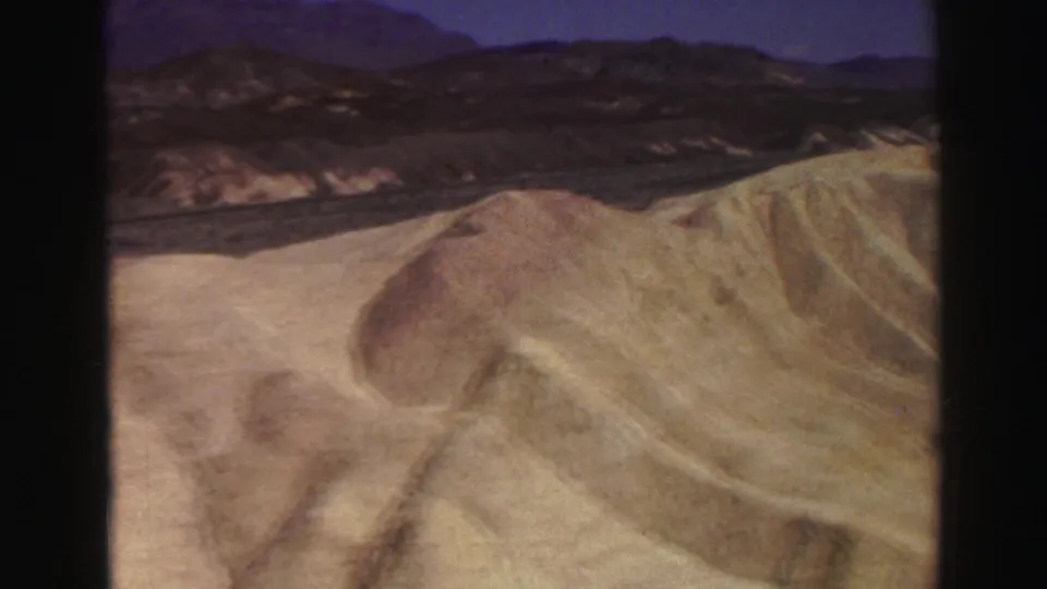 1969 8mm view of a rounded sandy hill form, layered ochre terrain, and distant dark mountains near the Lake Tahoe metadata location.
