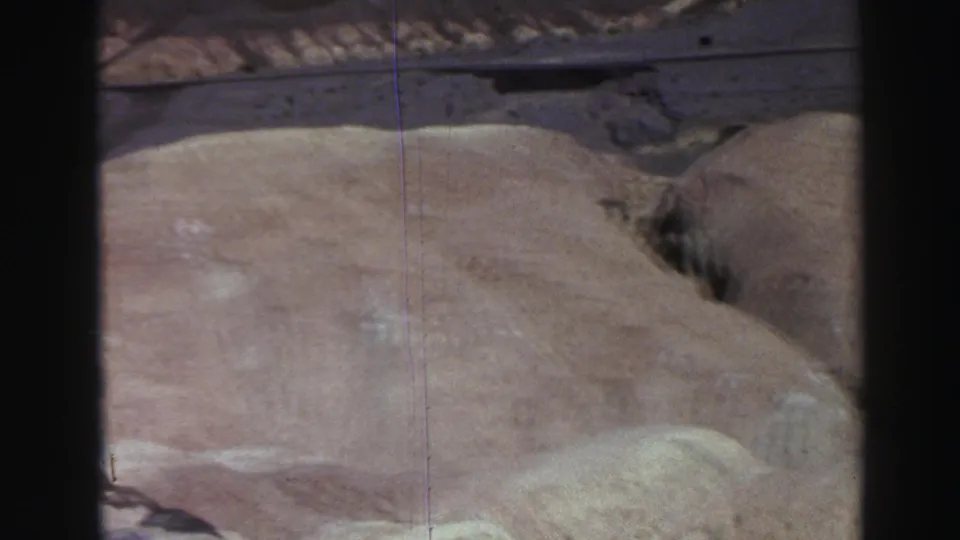 1969 Lake Tahoe-area canyon footage frame with a broad tan rock surface, muted color, and a dark crevice at the edge.