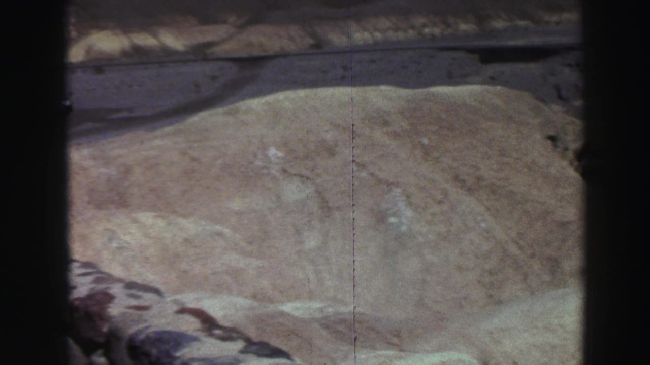 Pale hillside and stone retaining wall seen from above, with film gate edges visible.