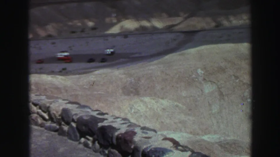 Lake Tahoe roadside overlook with period cars on a winding road above pale hills in 1969 home-movie footage.