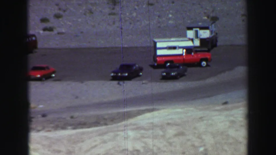 Lake Tahoe home-movie frame showing parked 1960s vehicles beside a gravel road and barren mountain slope.