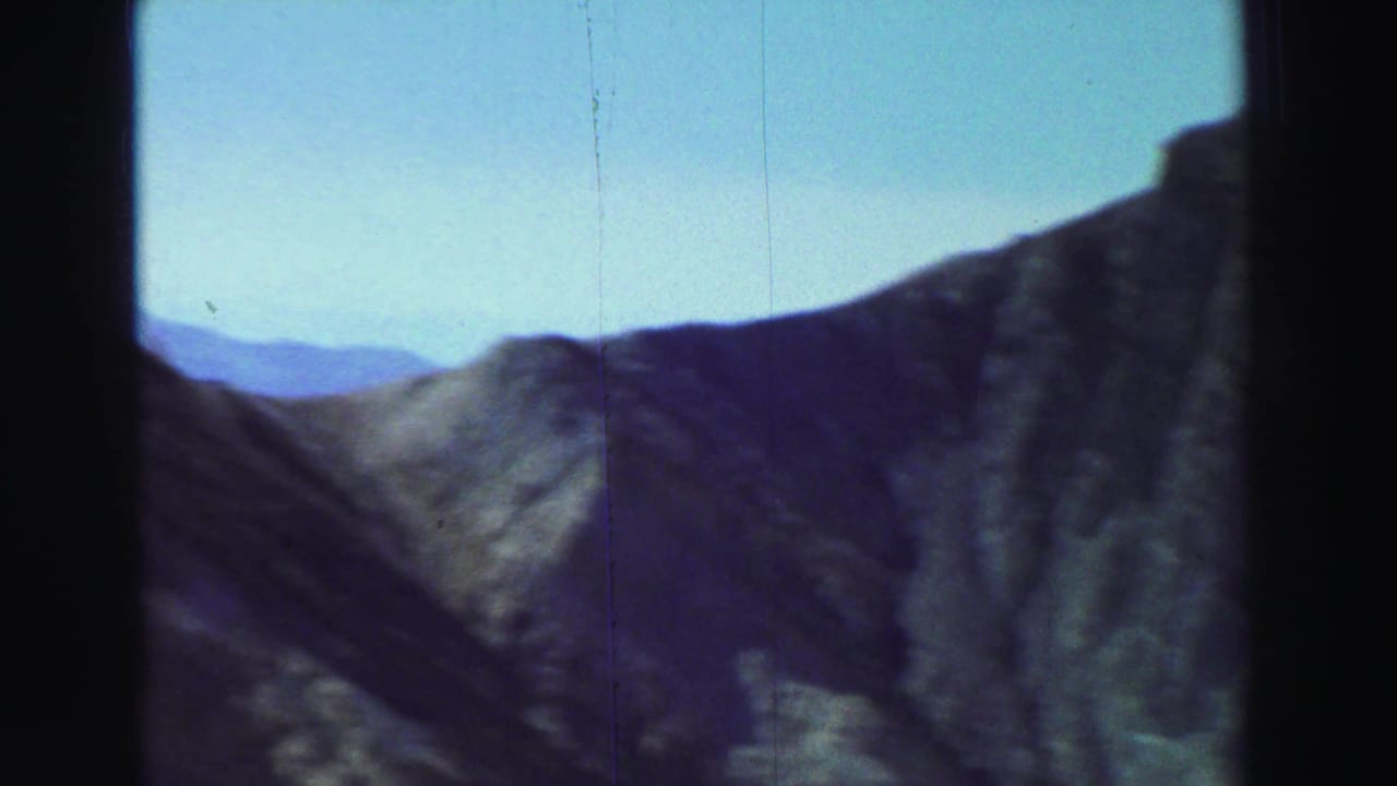 Rugged mountain ridge under a pale blue sky with dark film-frame edges.