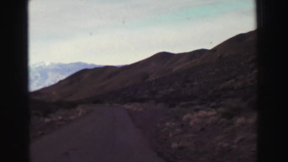 1969 8mm view from a moving car near Lake Tahoe, showing a paved road curving through dry hills toward distant mountains.