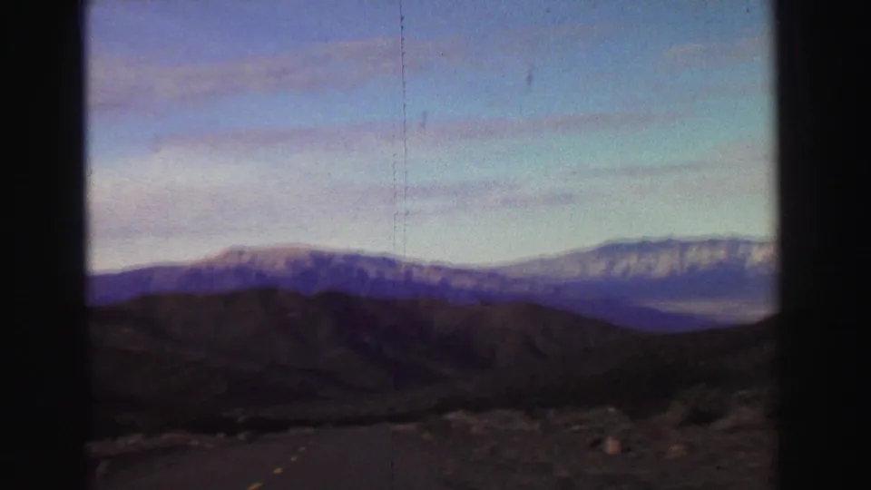 8mm passenger-view frame showing dark foreground hills and a distant snow-touched mountain range in the Lake Tahoe area.