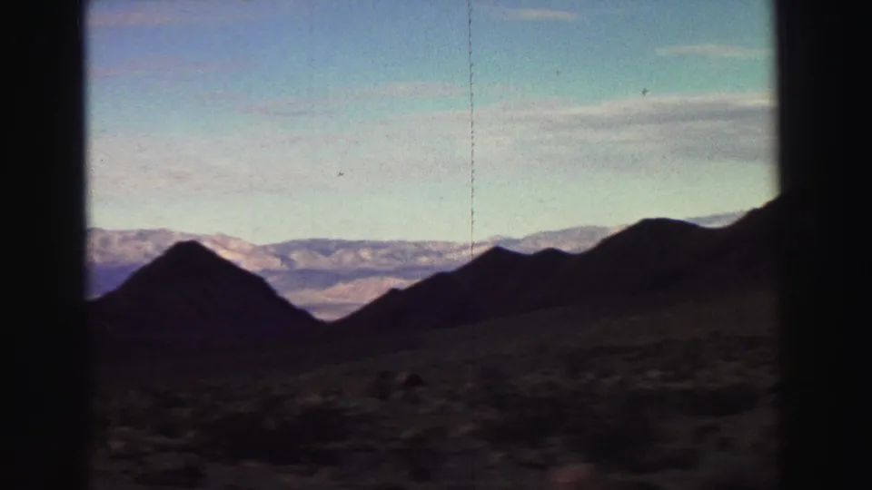 End frame from a 1969 Lake Tahoe-area drive, showing shadowed hills and a distant snowy mountain range under a clear sky.