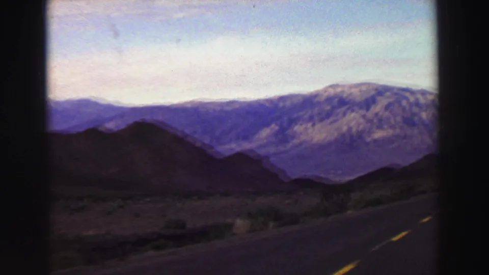 1969 Lake Tahoe-area 8mm frame with roadside pavement, scrubby terrain, silhouetted hills, and a broad mountain ridge.