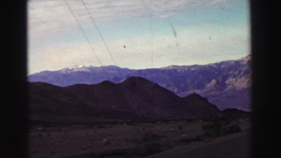 Lake Tahoe area 8mm footage from 1969 shows a roadside mountain landscape with dark hills, distant ridges, pale sky, and overhead utility lines.
