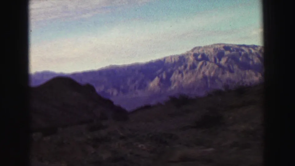 A 1969 8mm frame near Lake Tahoe shows dry hillside terrain, sparse brush, and a broad mountain ridge under a pale sky.