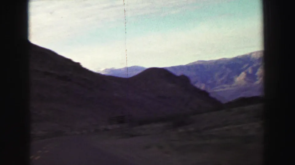 The final 1969 8mm frame shows a curving road through dry mountain terrain near Lake Tahoe, with layered ridges, sparse vegetation, and film scratches.