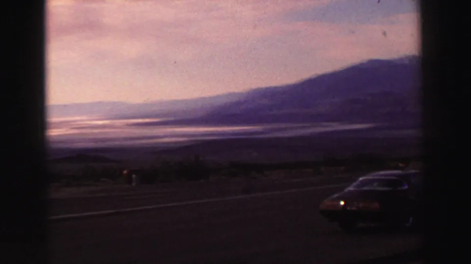 1969 Lake Tahoe area road view with a dark sedan at the edge of a scenic overlook and hazy mountains beyond.