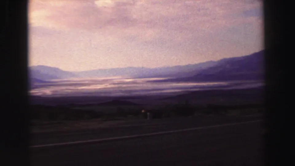 1969 8mm scenic road view near Lake Tahoe showing a broad hazy basin or valley framed by low mountains.