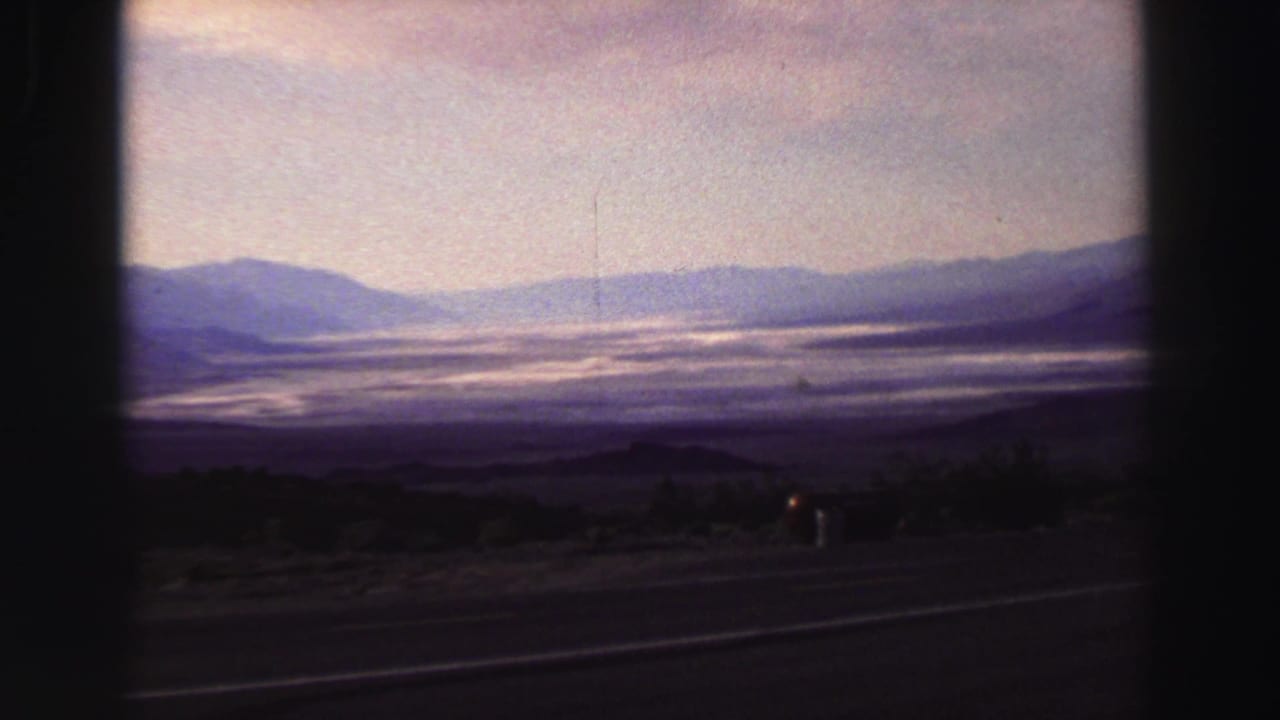 Hazy lake and mountain view from a roadside vantage with dark film-frame edges.