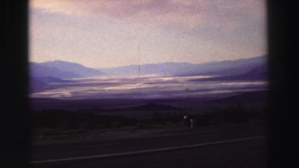 1969 Lake Tahoe roadside view with a hazy lake surface, layered mountains, and dark 8mm frame borders.