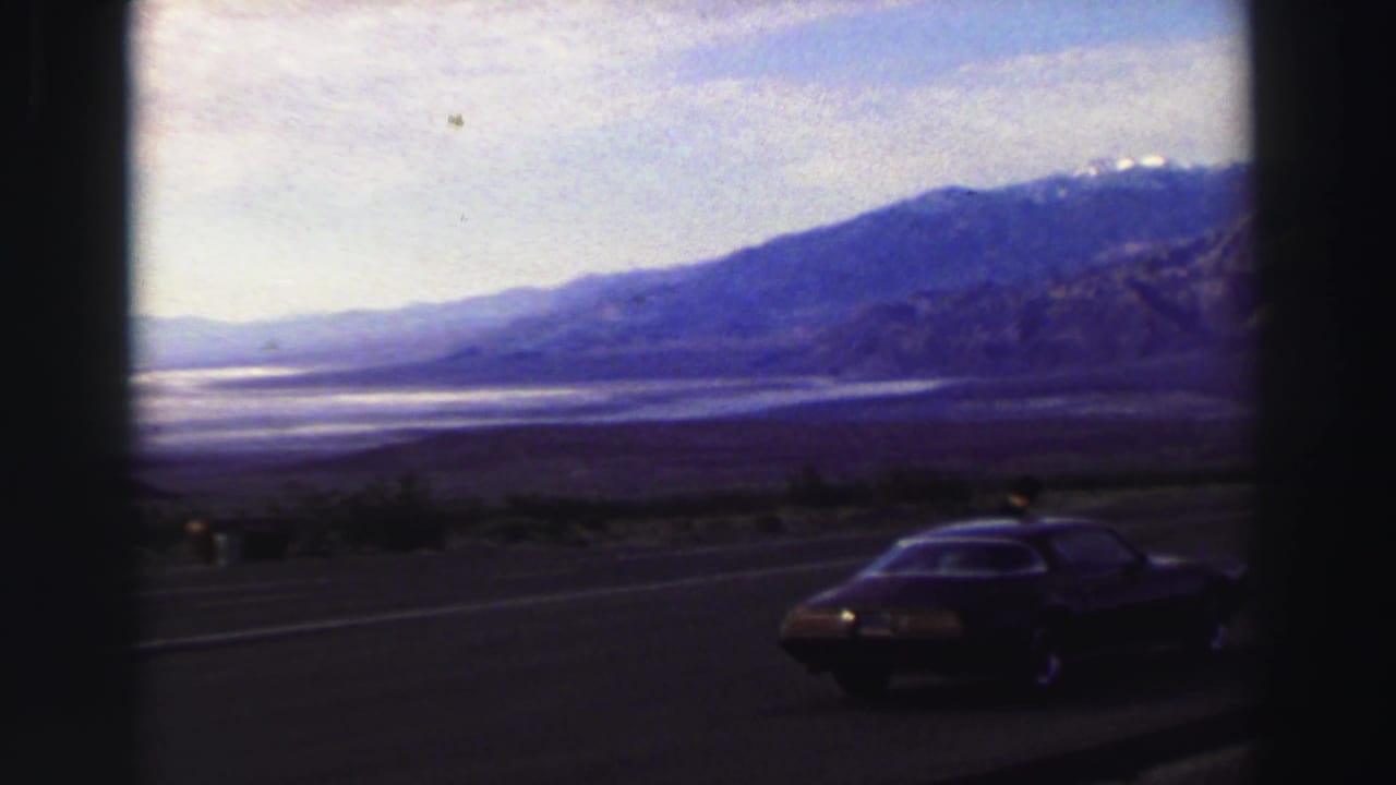 Dark coupe parked on a roadside with a valley and mountains beyond.