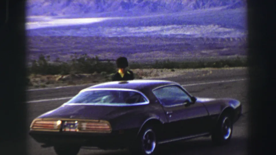 Final Lake Tahoe frame shows the parked Firebird and the person upright near the windshield against a hazy roadside landscape.
