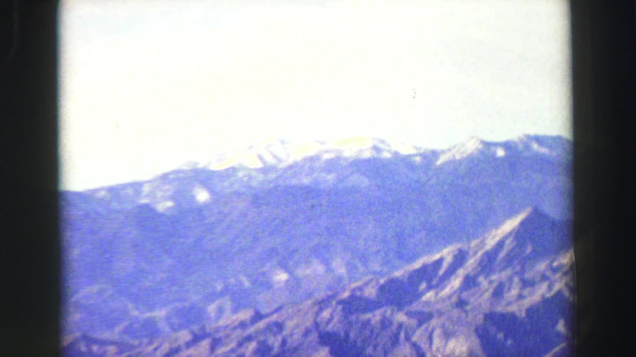 Distant snow-capped mountains seen through dark film borders under a pale sky.
