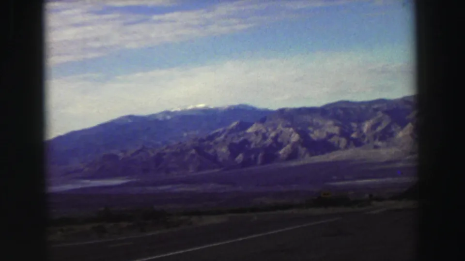 1969 8mm roadside view in the Lake Tahoe region, with a paved highway, low brush, valley floor, and distant mountains.