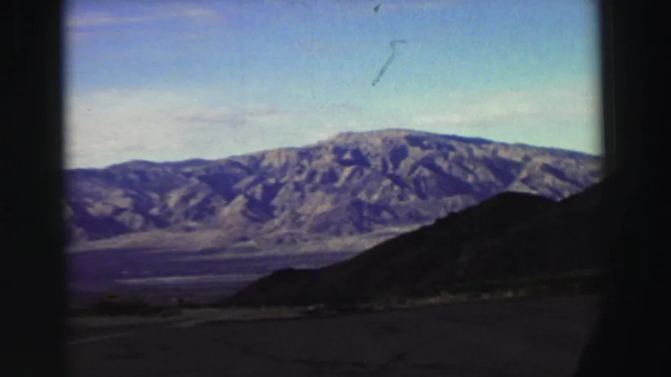 A Lake Tahoe-area mountain landscape appears through a vehicle window, with rocky ridges, a dark foreground hill, and road surface below.
