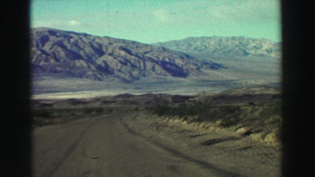 Paved road leading toward a distant mountain range across open scrubland.