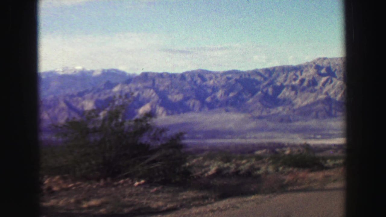 1969 Lake Tahoe-area home-movie frame showing a rugged mountain ridge across arid foreground shrubs and open sky.