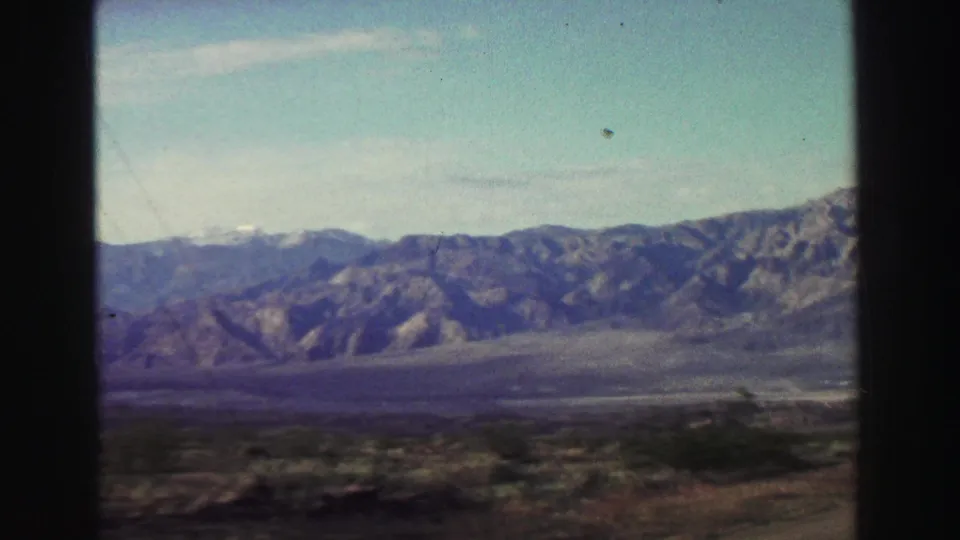 1969 Lake Tahoe-area road-travel view with distant mountains, open valley terrain, sparse shrubs, and visible film gate edges.