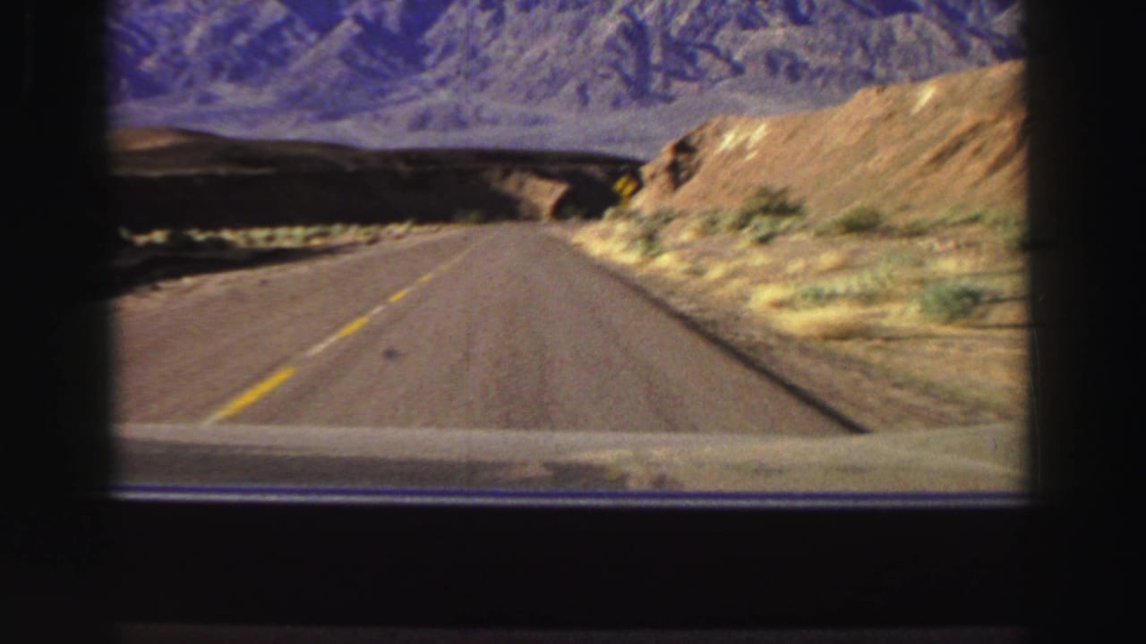Forward view along a paved mountain road with yellow center lines and distant rugged hills.
