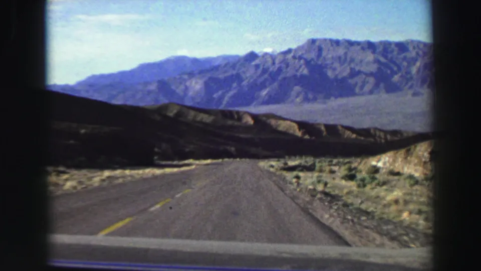 Passenger-view 8mm frame of a road crossing arid foothills toward mountains, consistent with the Lake Tahoe, California metadata.