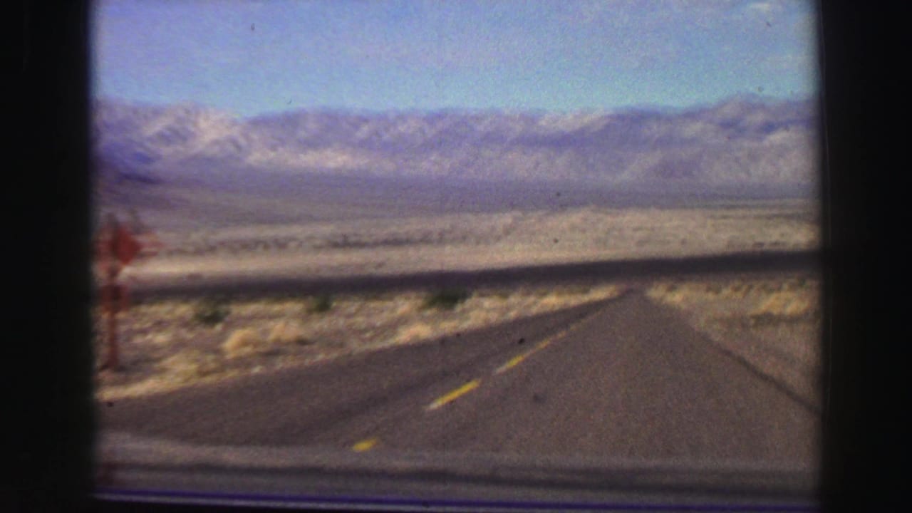 Straight desert road leading toward distant mountains under a blue sky.