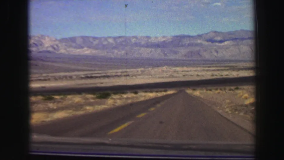 Vehicle-shot 8mm frame of a long desert road approaching mountains in the Lake Tahoe, California travel reel.