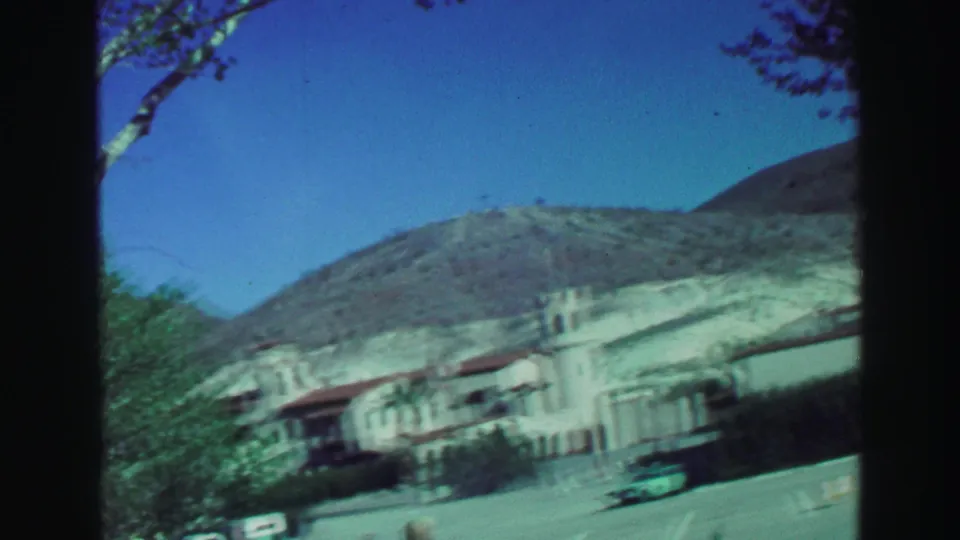 A pale Spanish-style building with tower forms appears against dry Lake Tahoe hills, with parked cars near the approach.