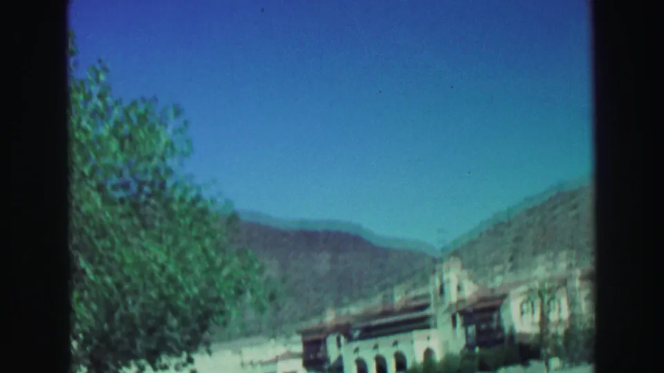 The moving 8mm view looks across trees and a dry mountain valley, with the pale Lake Tahoe building receding at the right edge.