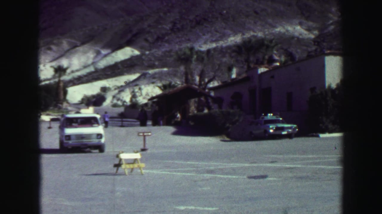 1969 Lake Tahoe resort parking area with a white van, low buildings, palm trees, and pale mountains in the background.