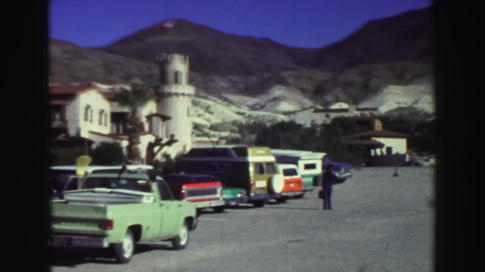 Green pickup, parked vans, tourists, and a towered resort building appear in a 1969 Lake Tahoe mountain village scene.