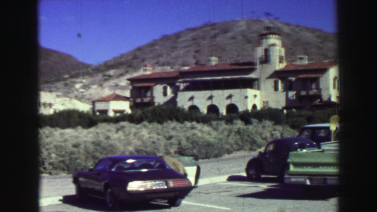 Spanish-style building beside a hillside with classic cars parked in the foreground.