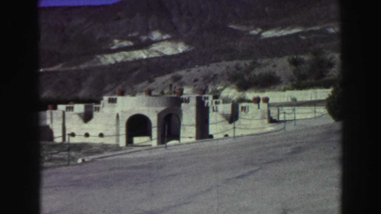 Spanish-style building beside a road with arched entries and hillside behind it.