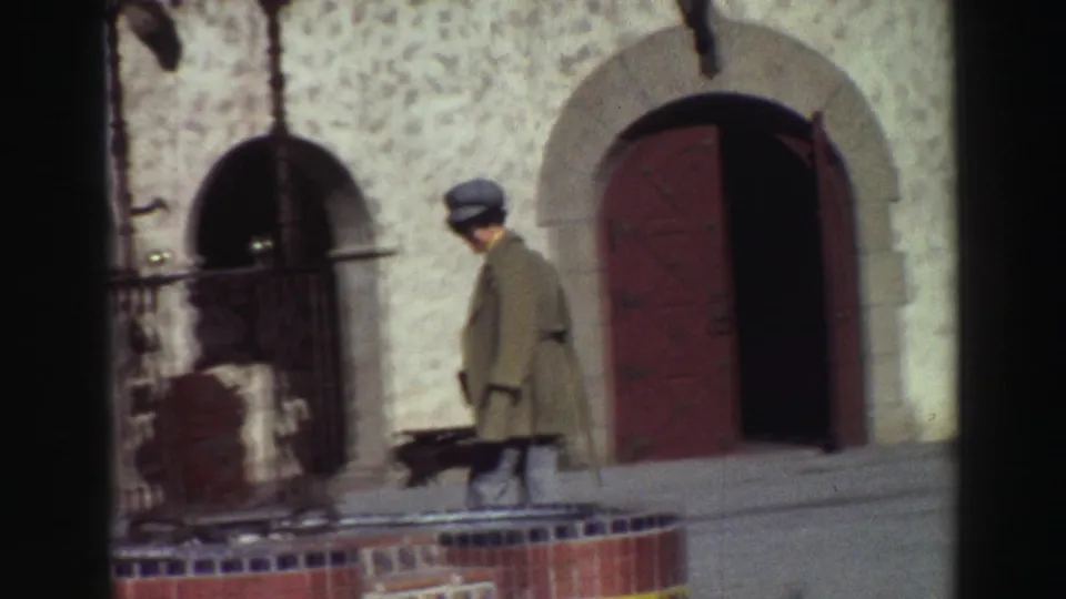 1969 Lake Tahoe courtyard view with a woman walking past arched stucco doorways and a tiled patio edge.