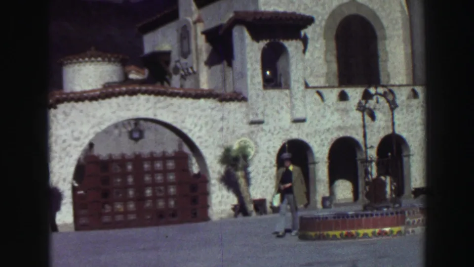 1969 Lake Tahoe frame showing the man farther across the walkway beside a fountain and arched stucco exterior.