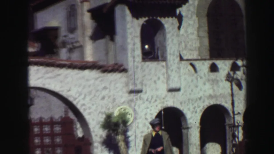 1969 Lake Tahoe frame with the man near the lower facade, arched openings, fountain edge, tile roof, and tower window.