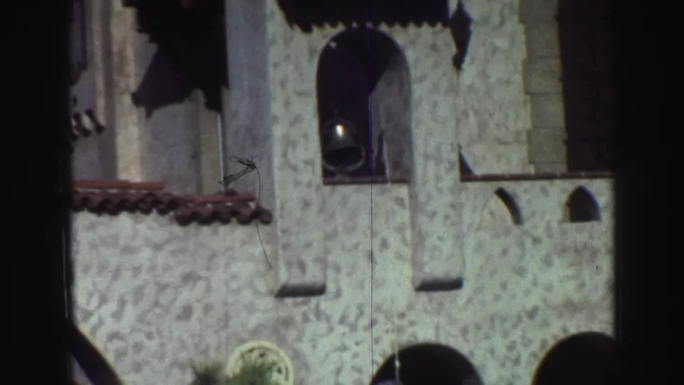 1969 Lake Tahoe-area 8mm frame showing a white textured building facade with arched openings, a bell, red roof tiles, and dark film edges.